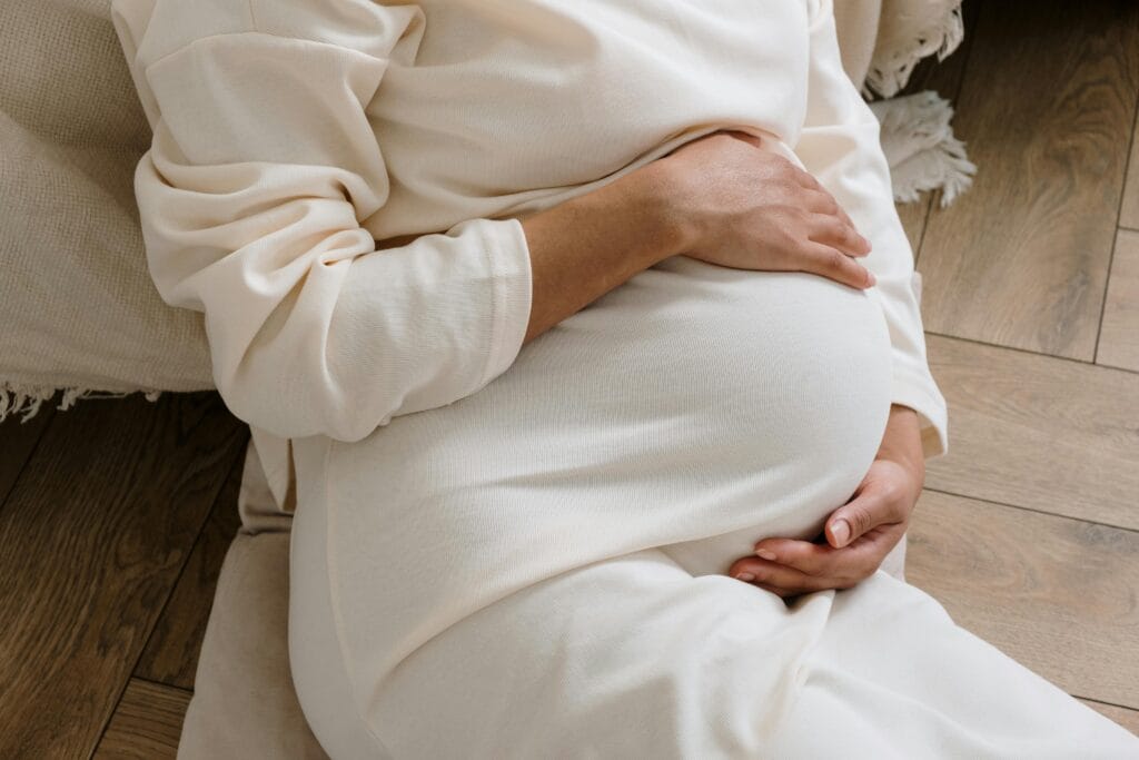 A serene moment of a pregnant woman in a cozy white dress holding her belly.